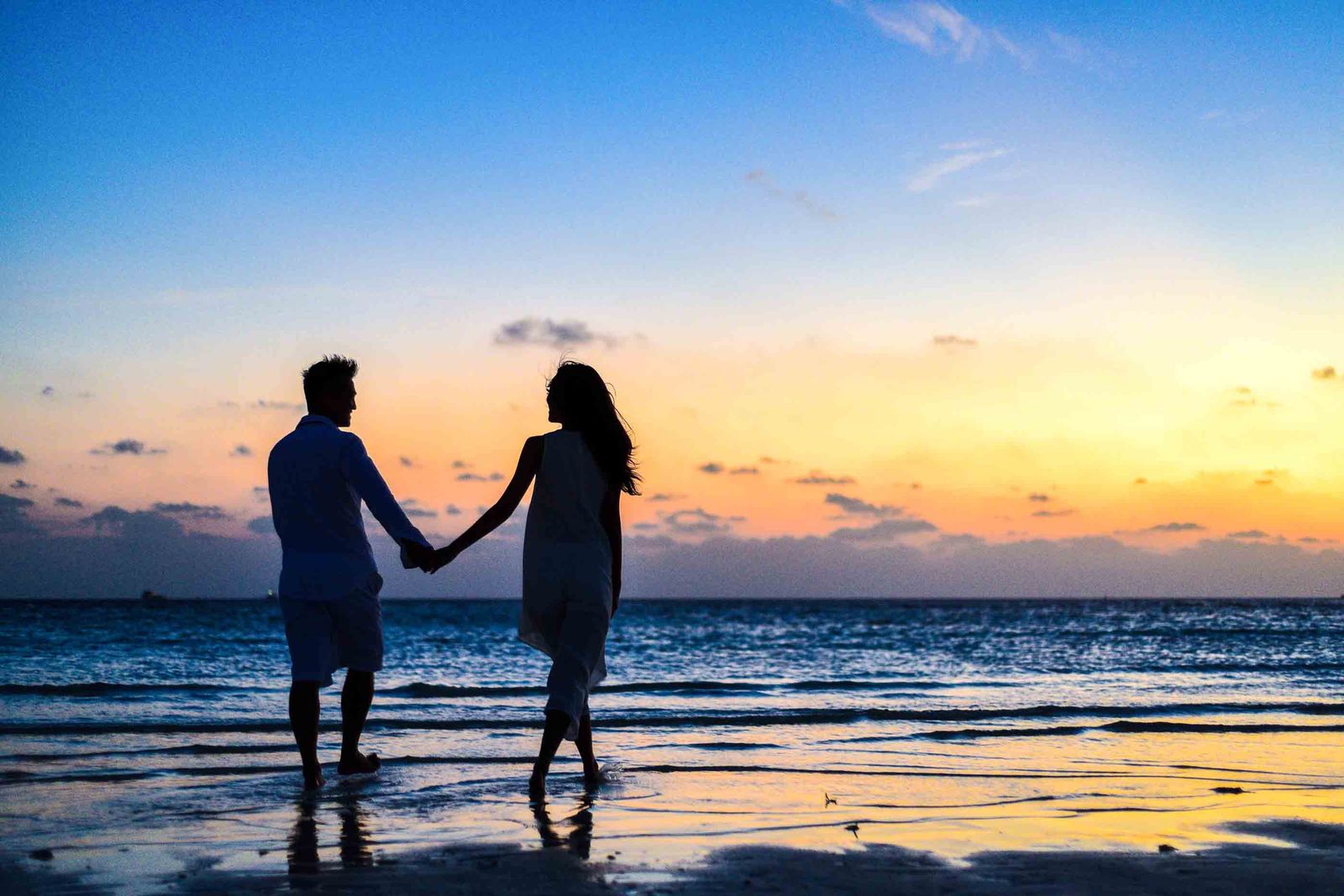Un couple main dans la main face à la mer au coucher du soleil